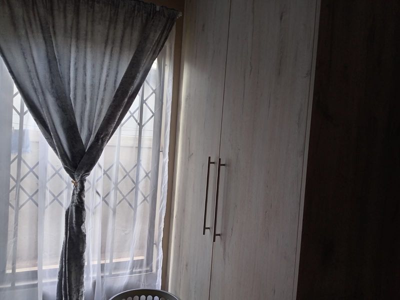 A bedroom featuring light-toned built-in cupboards and a window fitted with a security gate.
