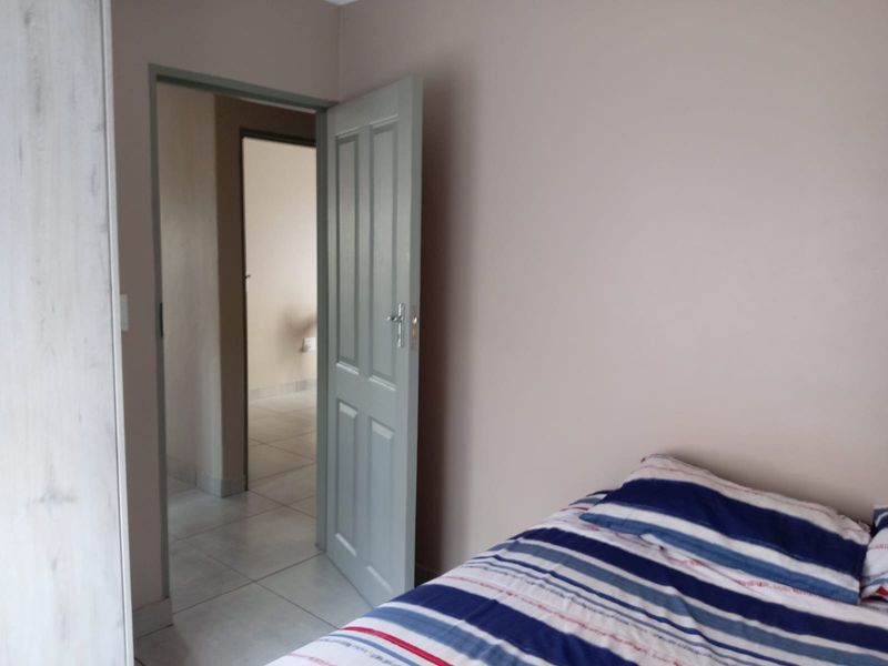 A bedroom featuring tiled flooring and a built-in cupboard, with an open doorway leading to an adjacent hallway.