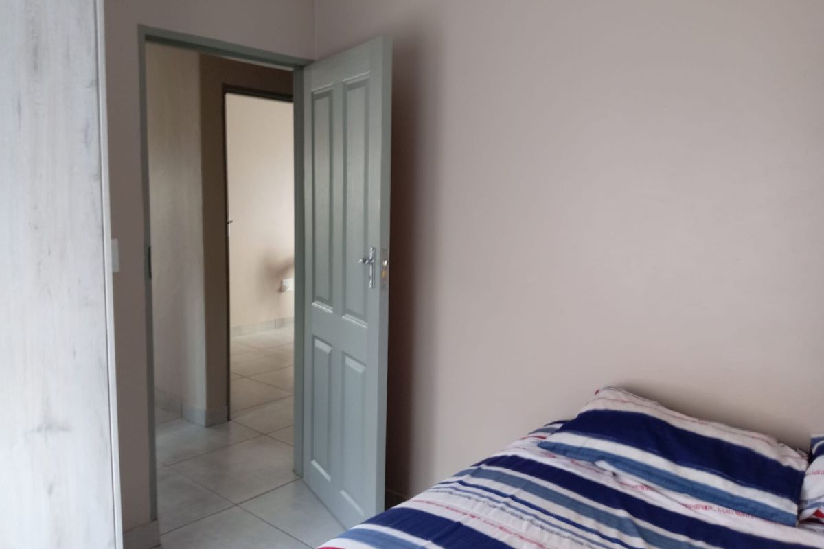 A bedroom featuring tiled flooring and a built-in cupboard, with an open doorway leading to an adjacent hallway.