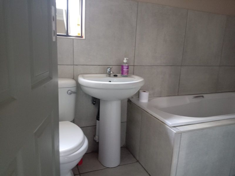 A functional bathroom featuring a pedestal basin, a standard toilet, and a built-in bathtub with neutral wall and floor tiling.