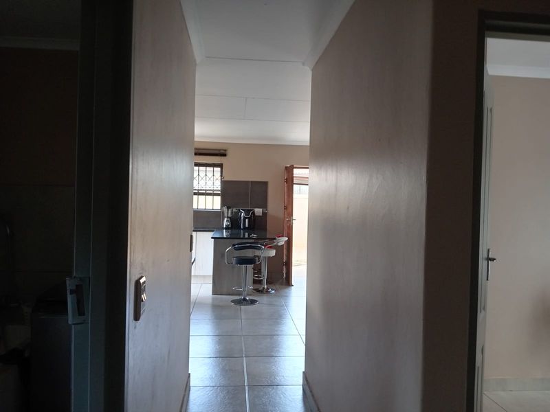 A view through a hallway leading into a kitchen area featuring tiled flooring and built-in cabinetry.