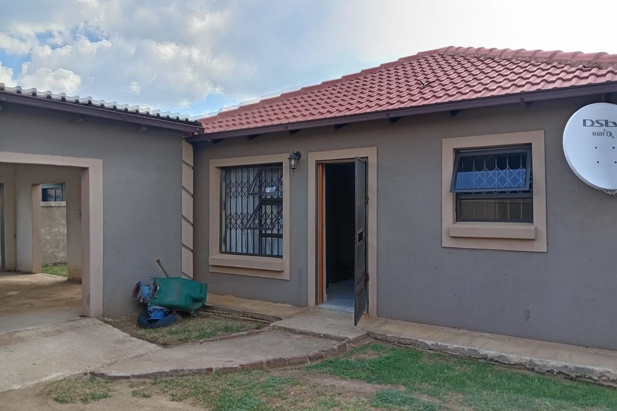 Rear exterior view of the house featuring a tiled roof, security gates on windows and doors, and a concrete pathway leading to the entrance.