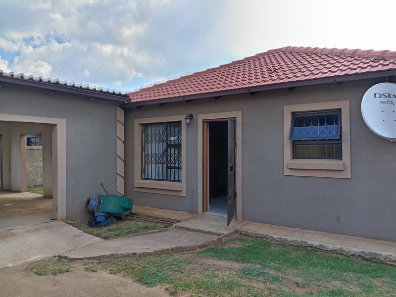 Rear exterior view of the house featuring a tiled roof, security gates on windows and doors, and a concrete pathway leading to the entrance.