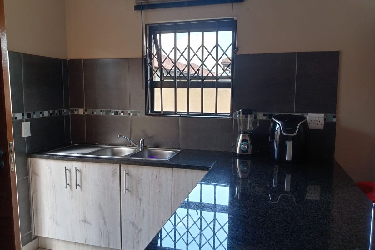 A functional kitchen featuring granite countertops, a stainless steel double sink, and modern wood-finish cabinetry with a tiled backsplash.