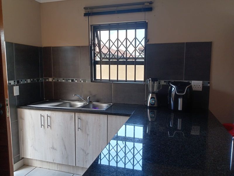 A functional kitchen featuring granite countertops, a stainless steel double sink, and modern wood-finish cabinetry with a tiled backsplash.