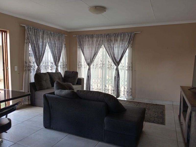 A living room featuring tiled flooring and sliding glass doors with security gates, providing access to the exterior.