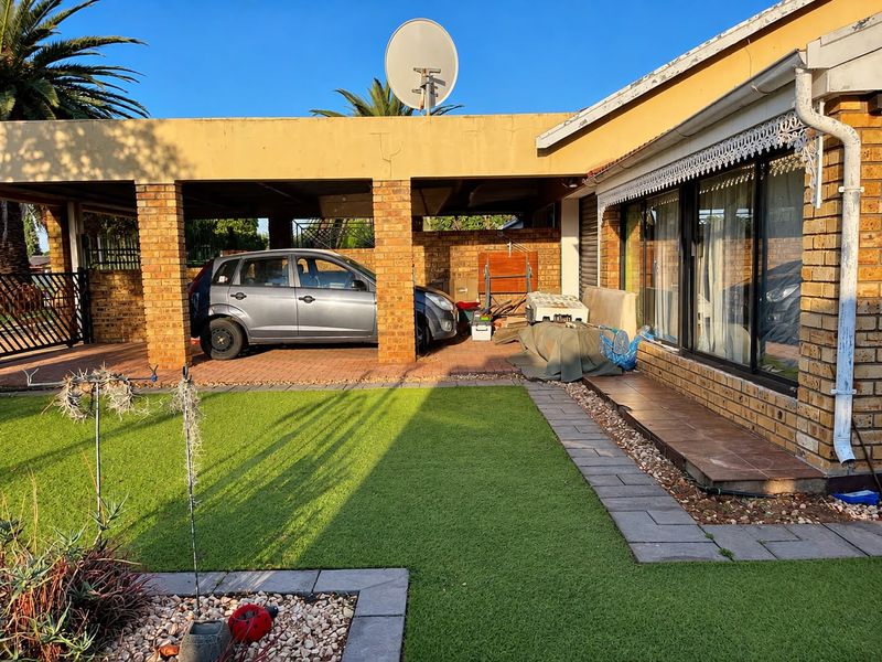 Rear exterior view of the townhouse featuring a brick carport, artificial lawn, and paved walkway area.