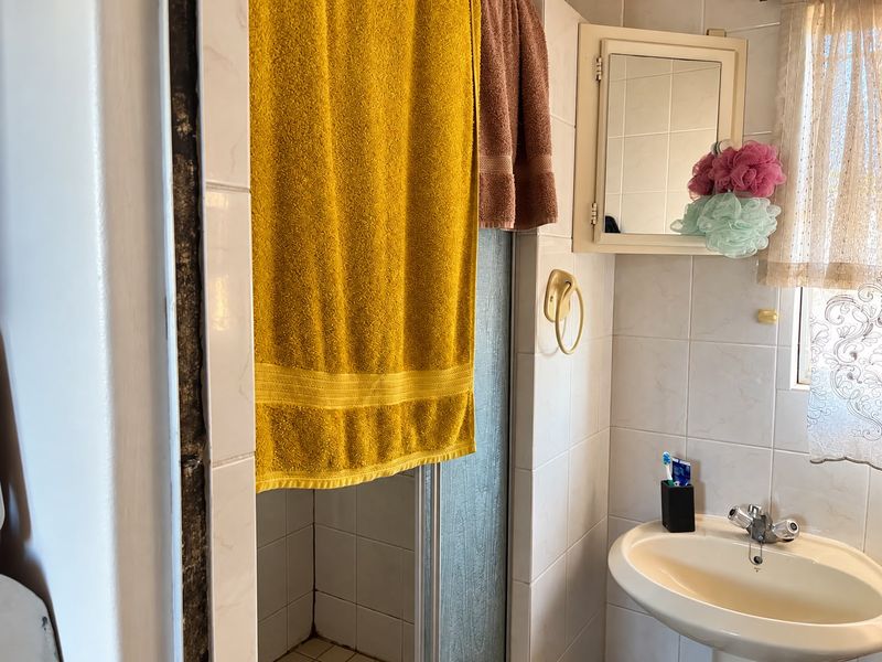 A compact bathroom featuring a pedestal sink, shower enclosure, and wall-mounted medicine cabinet with tiled wall finishes.