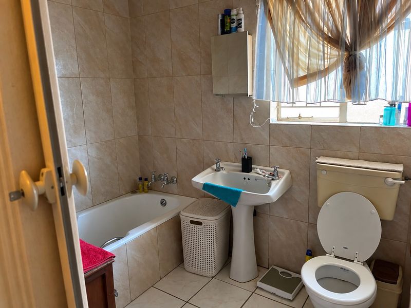 A functional bathroom featuring a pedestal washbasin, bathtub, and toilet with full-height wall tiling and tiled flooring.