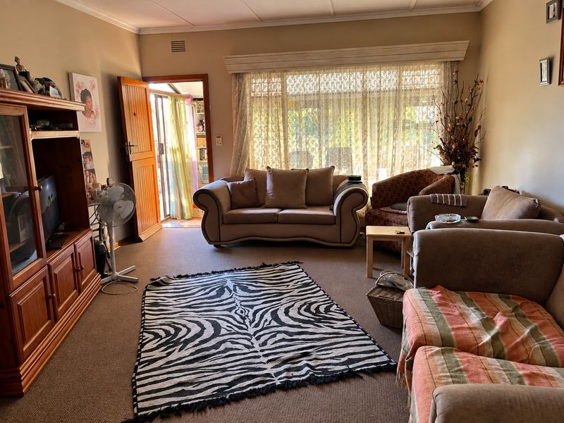 A spacious living room featuring carpeted flooring, a large window with natural light, and direct access to an adjoining room.