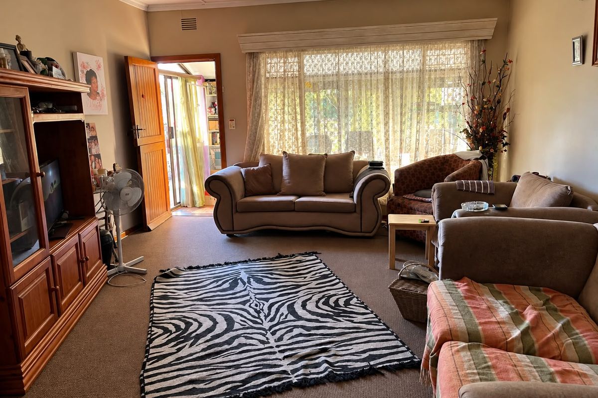 A spacious living room featuring carpeted flooring, a large window with natural light, and direct access to an adjoining room.
