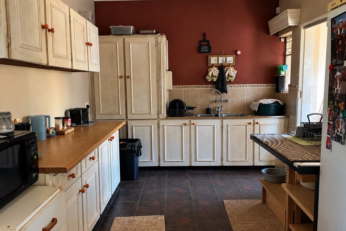 A functional kitchen featuring traditional built-in cabinetry, laminate countertops, a double basin sink, and tiled flooring with a contrasting feature wall.