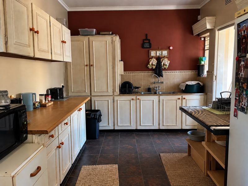 A functional kitchen featuring traditional built-in cabinetry, laminate countertops, a double basin sink, and tiled flooring with a contrasting feature wall.
