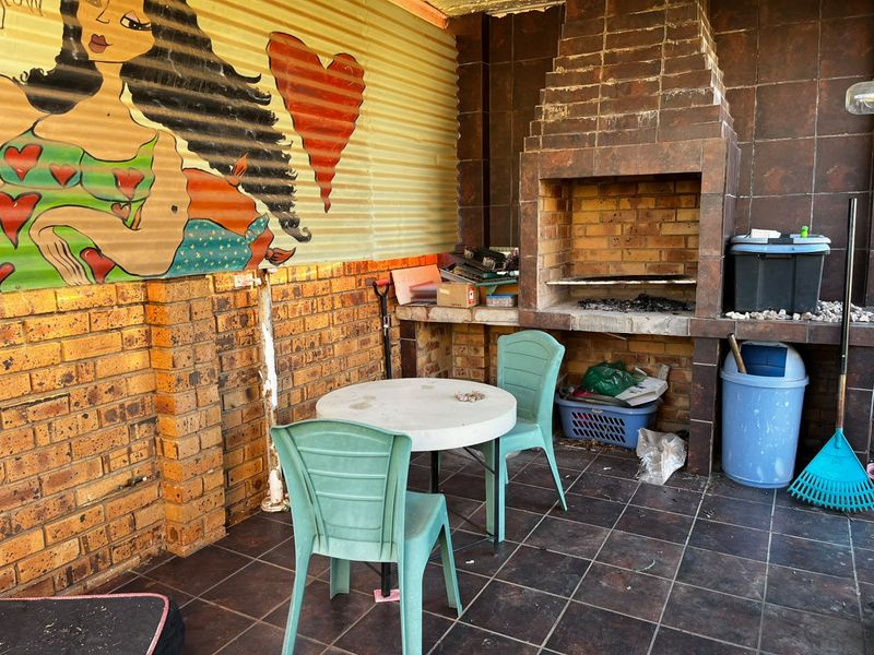 Covered patio area featuring a built-in brick braai, tiled flooring, and corrugated metal wall cladding with decorative mural.