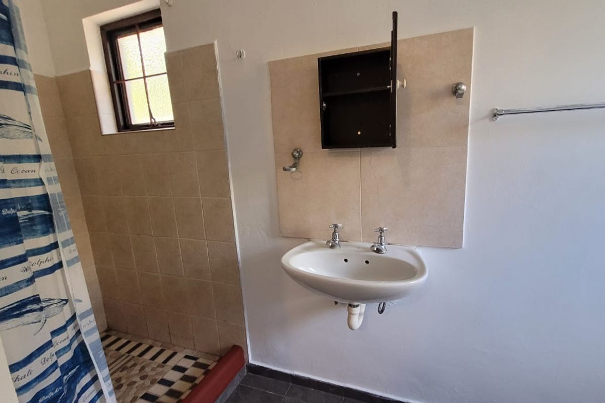 A functional bathroom featuring a wall-mounted basin, tiled shower area, and window, requiring minor cosmetic updates to the fixtures and finishes.