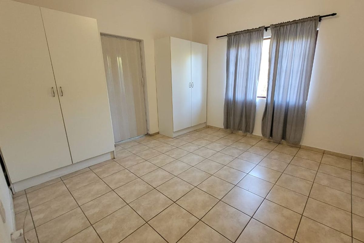 A bright, empty bedroom featuring neutral tiled flooring and built-in cupboards, offering a clean and versatile space ready for personalization.