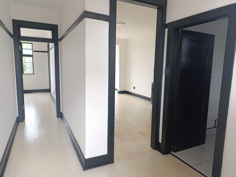 A bright, empty hallway featuring painted timber trim and light-toned timber flooring, providing access to multiple rooms within the apartment.