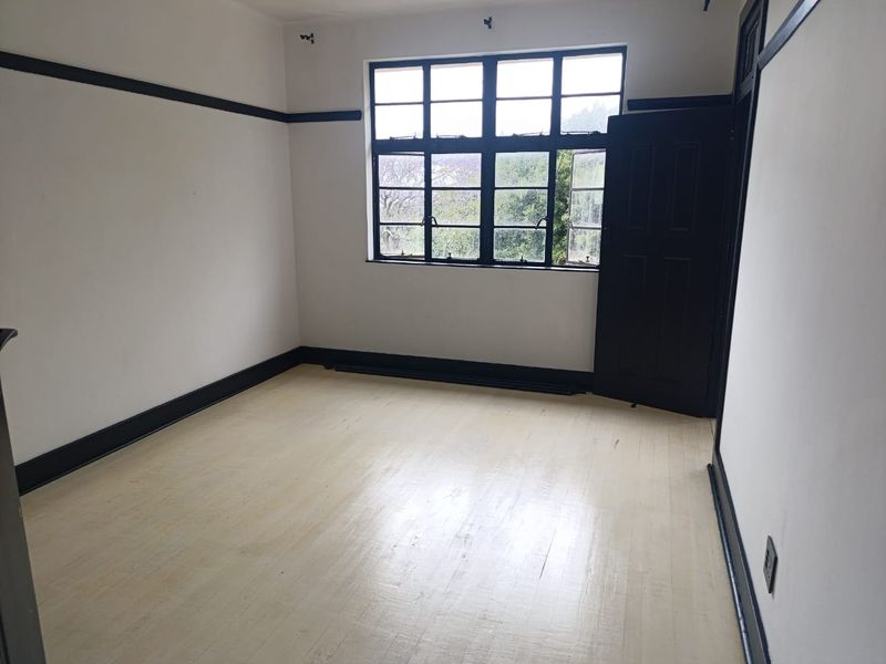 An empty bedroom featuring timber flooring, dark-painted trim, and a multi-pane window, offering a blank canvas for renovation or interior design.