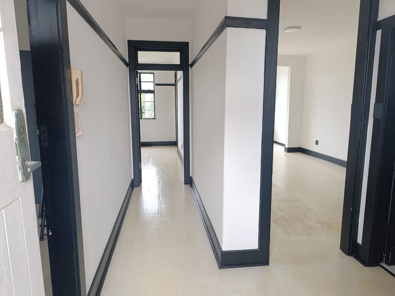 A bright, empty hallway featuring painted timber trim and original timber flooring, providing access to multiple rooms within the apartment.
