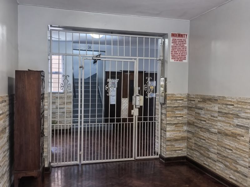 Apartment building entrance foyer featuring parquet flooring, stone-effect wall cladding, and a secure metal gate leading to the stairwell.