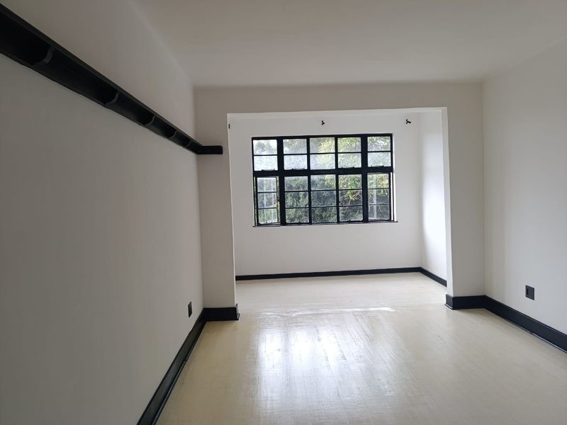 An empty, bright living area featuring painted timber floors, black-framed windows, and contrasting black skirting boards, offering a clean, neutral canvas.
