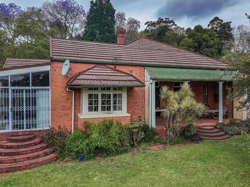 Rear view of a classic brick house featuring a covered patio, tiled roof, and established garden surroundings.