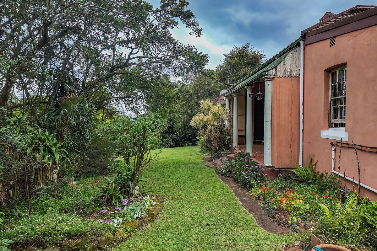 Rear view of the property featuring a covered veranda with classical columns, sash windows, and a well-established garden with mature trees.