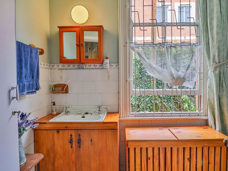 A dated bathroom featuring a wooden vanity cabinet, tiled splashback, and a window with security bars, offering potential for modernization.