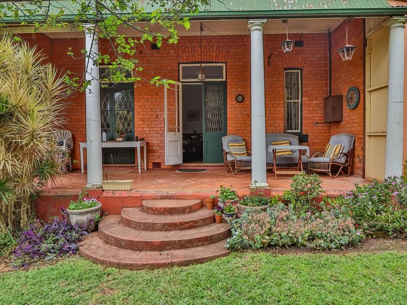 A charming covered patio featuring classic brickwork, concrete columns, and terracotta flooring, offering a traditional outdoor living space overlooking the garden.