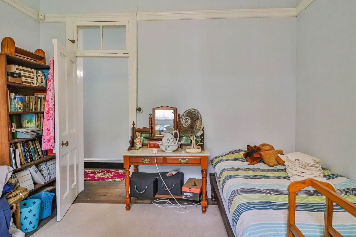A bedroom featuring original timber flooring, a classic door with a transom window, and traditional picture rail detailing.