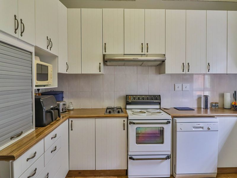 Functional kitchen featuring white cabinetry, wood-look countertops, tiled backsplash, and integrated appliances including a dishwasher and extractor fan.