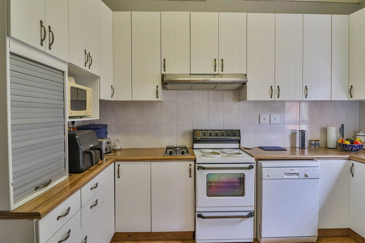 Functional kitchen featuring white cabinetry, wood-look countertops, tiled backsplash, and integrated appliances including a dishwasher and extractor fan.
