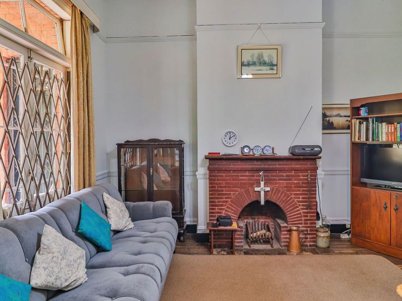 A cozy living room featuring a classic brick fireplace, timber flooring, and traditional picture rails, offering a warm and inviting atmosphere.