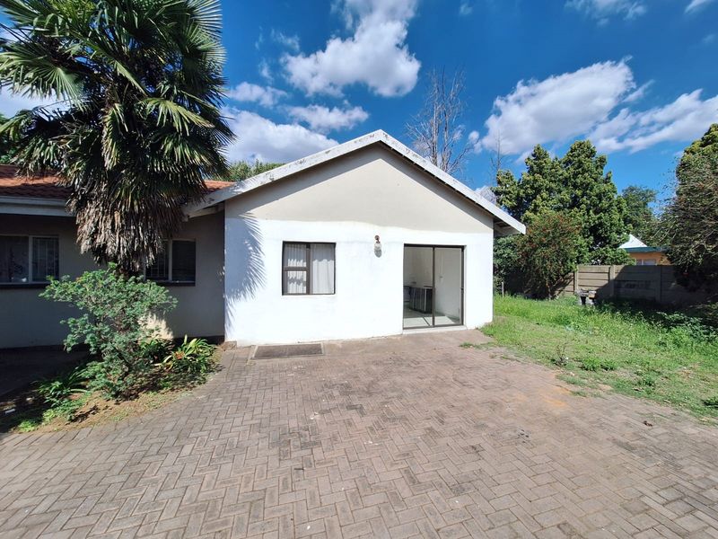 Rear view of the property featuring a paved patio area, sliding door access, and a large garden space with boundary walling.
