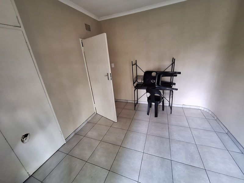 A simple bedroom featuring tiled flooring and a built-in cupboard with visible damage to the door panel.