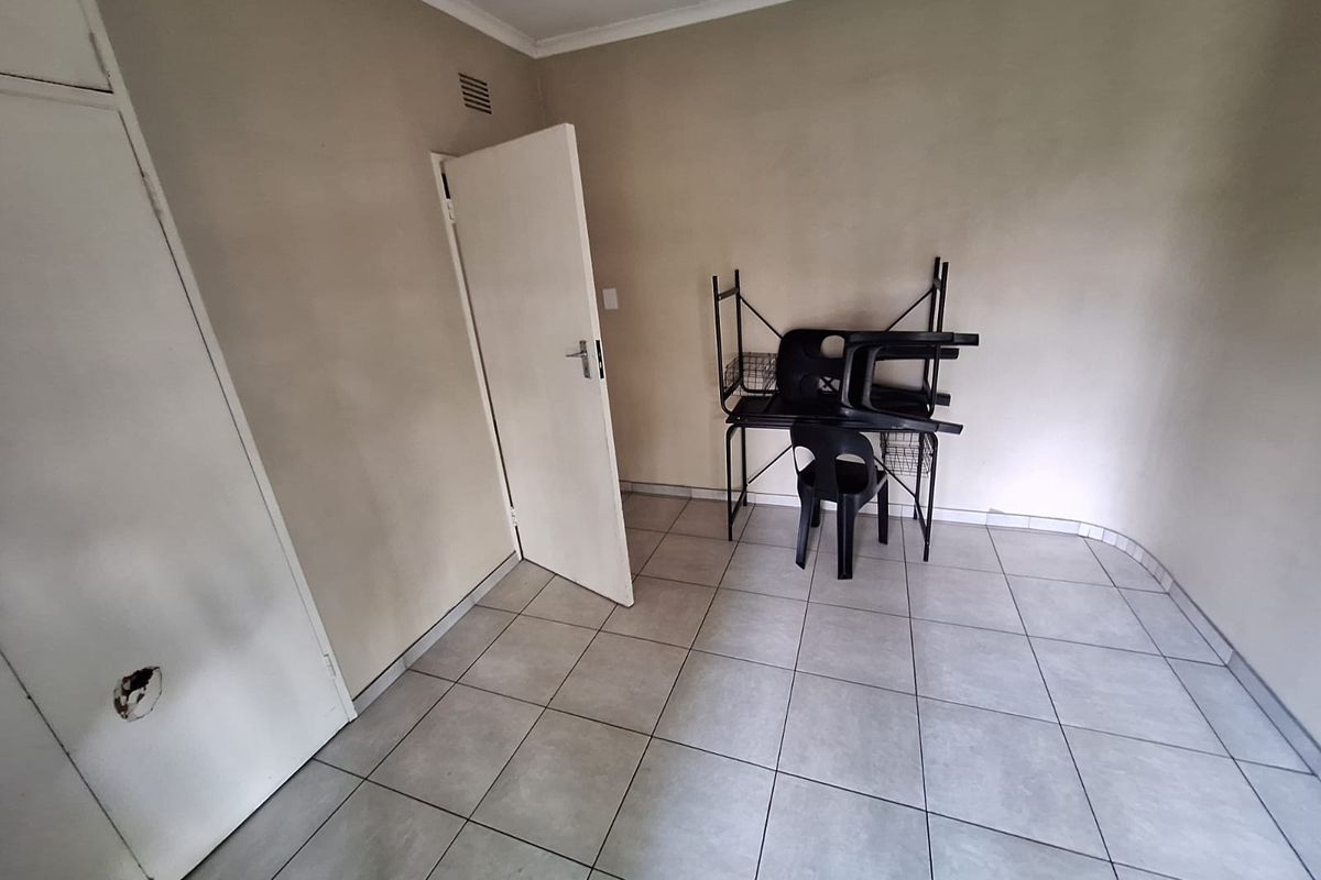 A simple bedroom featuring tiled flooring and a built-in cupboard with visible damage to the door panel.