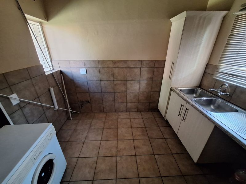A functional laundry area featuring built-in cabinetry, a double sink, tiled splashbacks, and tiled flooring, requiring minor maintenance to the wall finishes.