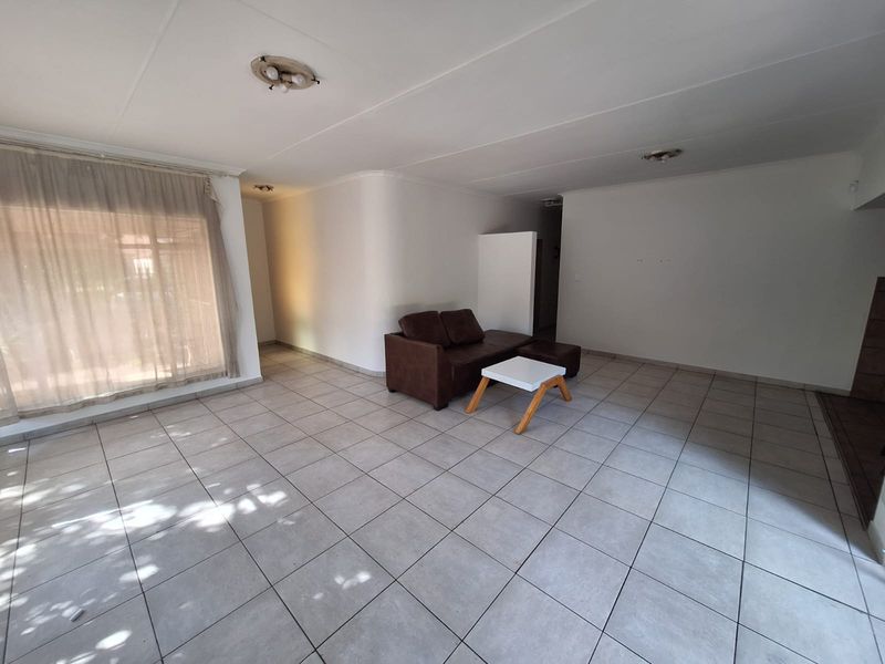 A spacious living area featuring neutral tiled flooring and simple ceiling lighting, offering a blank canvas for interior design updates.