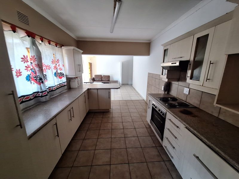 Functional kitchen featuring built-in cabinetry, laminate countertops, electric hob, oven, and extractor fan with tiled flooring and backsplash.