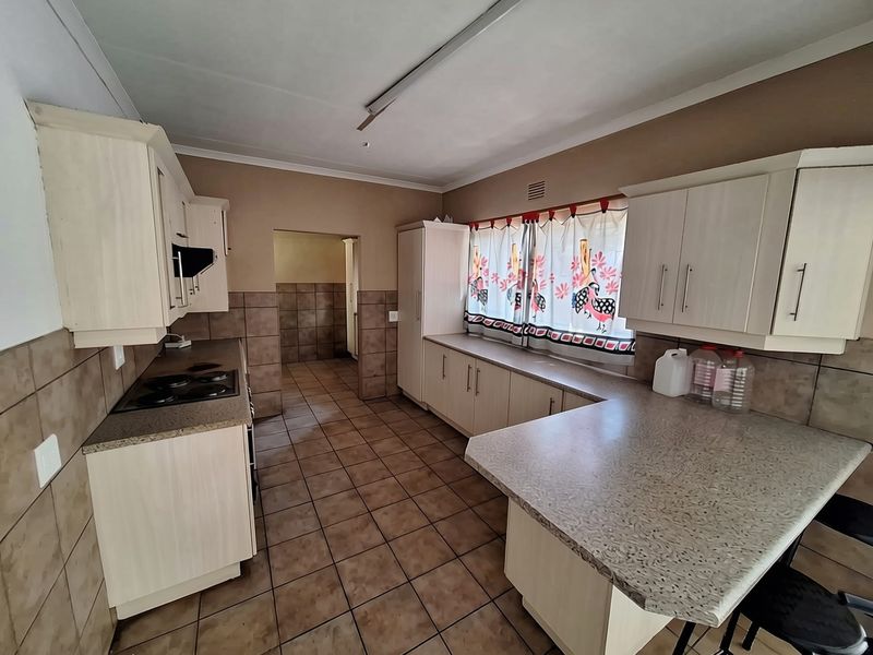 A functional kitchen featuring built-in cabinetry, laminate countertops, an electric hob, and tiled flooring with wall-mounted splashback tiling.