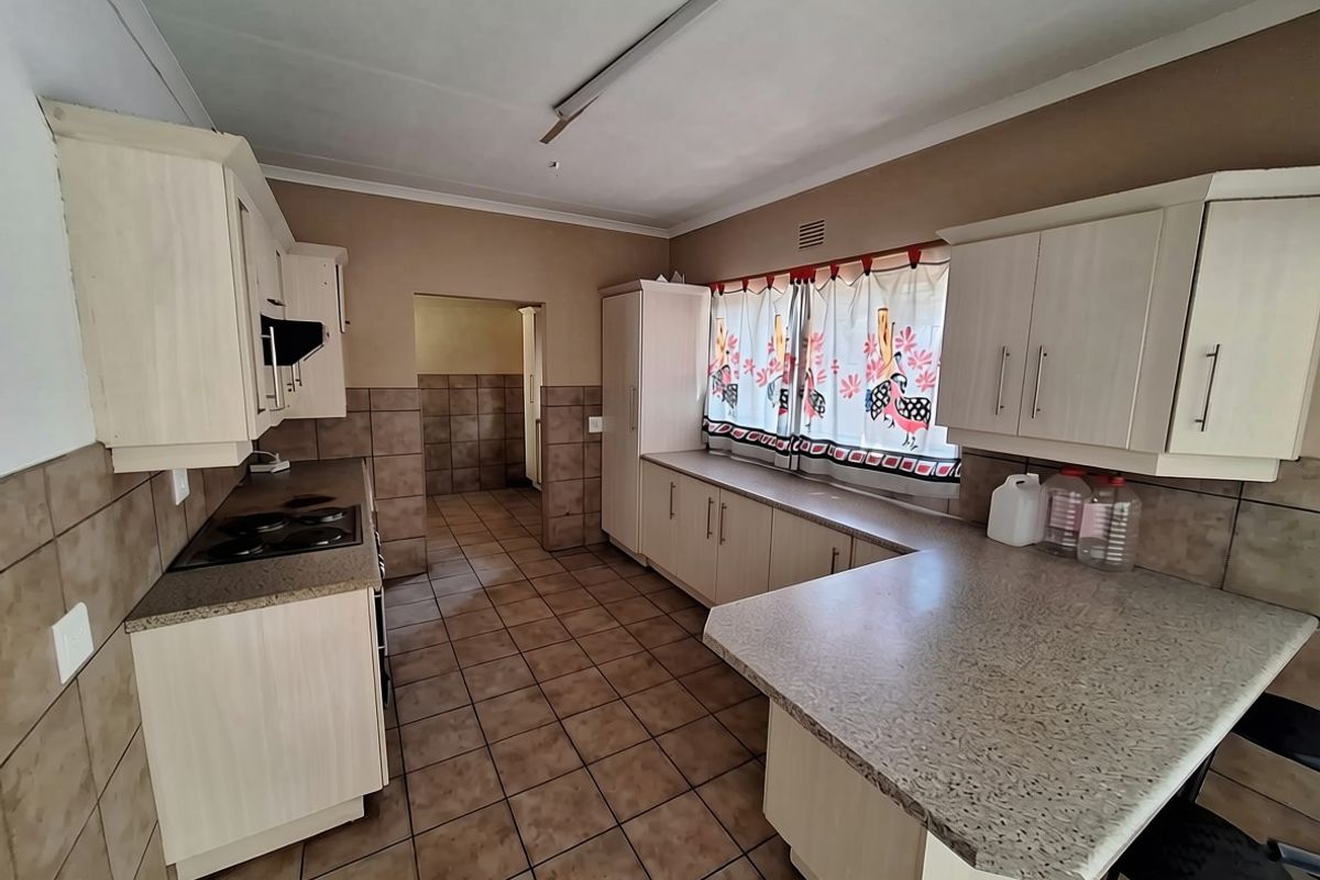 A functional kitchen featuring built-in cabinetry, laminate countertops, an electric hob, and tiled flooring with wall-mounted splashback tiling.