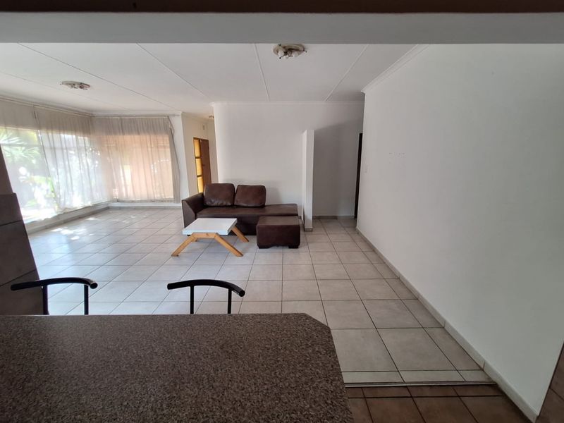 Spacious open-plan living area featuring tiled flooring, a breakfast bar with granite countertop, and large windows allowing for ample natural light.