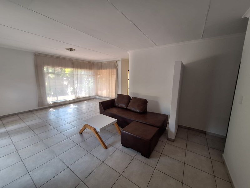 A spacious living area featuring neutral tiled flooring, a partition wall, and large corner windows that provide ample natural light.