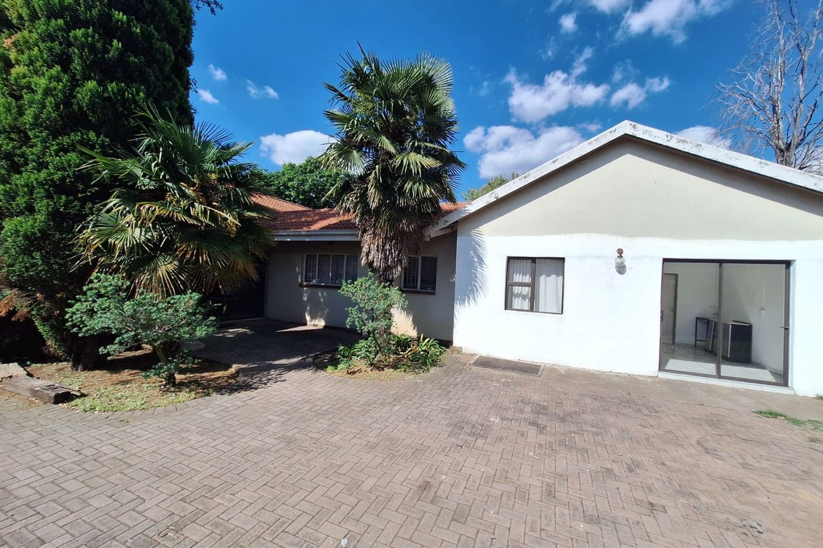 Rear exterior view of the house featuring a paved courtyard area, sliding glass door access, and established garden landscaping.