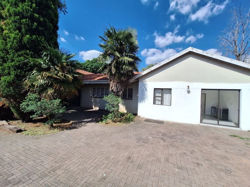 Rear exterior view of the house featuring a paved courtyard area, sliding glass door access, and established garden landscaping.