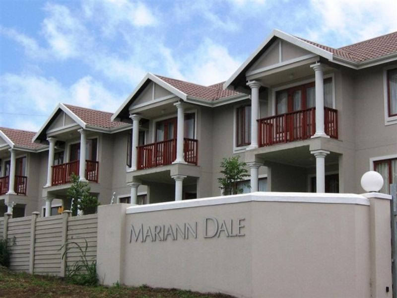 Front elevation of the Mariann Dale townhouse complex featuring multi-level units with balconies, decorative columns, and a prominent boundary wall.