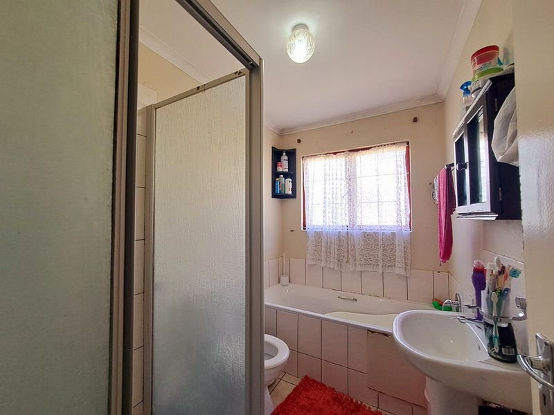 A functional bathroom featuring a shower enclosure, bathtub, pedestal basin, and toilet, with dated finishes and visible wear on the bathtub panel.