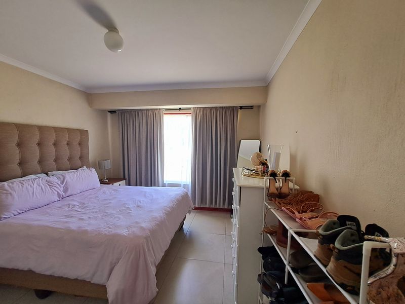 A functional bedroom featuring tiled flooring, neutral wall finishes, and window curtain tracks, providing a comfortable and well-lit sleeping space.