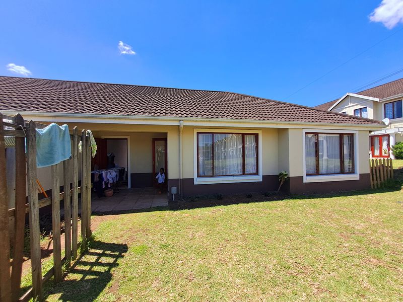 Rear view of the townhouse featuring a covered patio, tiled roof, and a private garden area with established lawn.