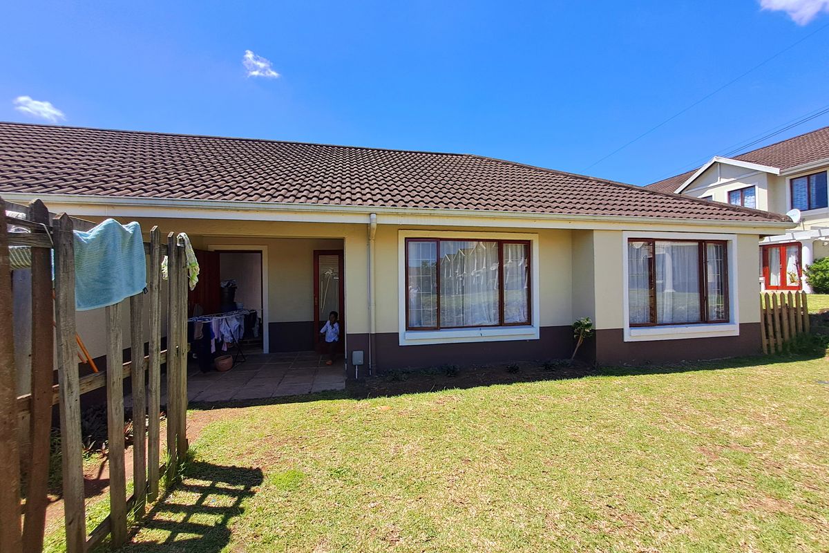 Rear view of the townhouse featuring a covered patio, tiled roof, and a private garden area with established lawn.